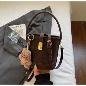 Gros plan détaillé du sac seau vintage en cuir marron avec boucle dorée et breloque ours