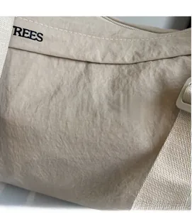 Close-up of beige canvas crossbody bag with white stitching and brand text REES
