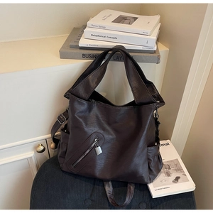 Detailed view of dark brown leather tote bag with silver lock and zip pocket in warm indoor light