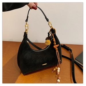 Detail of black suede dumpling bag with gold zipper and colorful beaded tassel charm