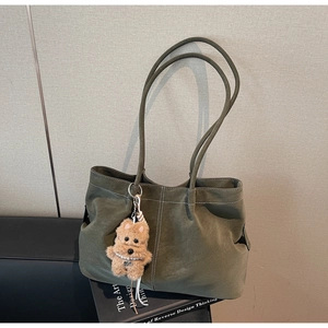 Macro detail of dark green suede tote bag with contrast stitching and plush puppy charm