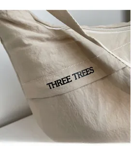 Close-up of beige canvas shoulder bag with Three Trees logo and smooth zipper detail