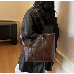 Détail d'un grand sac cabas marron foncé en cuir huilé brillant avec logo doré