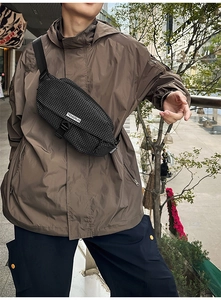 Detail of waterproof nylon crossbody bag with woven label on a brown outdoor jacket