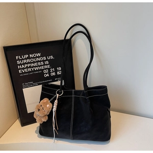 Detail of black leather tote bag with white contrast stitching and plush bear charm