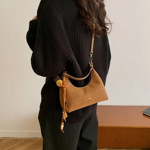 Detail of dark brown suede dumpling bag with gold logo and bohemian tassel charm