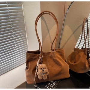 Detailed close-up of brown suede tote bag featuring white contrast stitching and bear charm