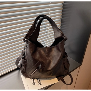 Detail of dark brown tote bag showing smooth faux leather texture and metallic zippers