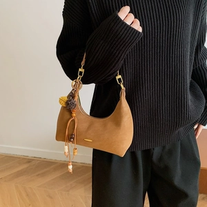 Detail of a brown half-moon bag featuring a decorative ethnic tassel with plush balls and beads