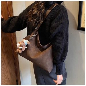Detail view of large dark brown tote bag with embossed pattern and cute bear charm