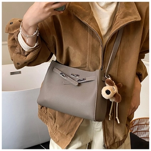 Detail of taupe lychee leather crossbody bag with metal lock and plush dog charm accessory