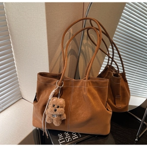 Detail of dark brown tote bag with contrast stitching and plush bear charm decoration