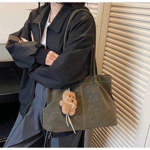 Detail of olive green suede tote bag with white contrast stitching and teddy bear charm