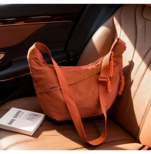 Orange nylon crescent crossbody bag with woven zipper detail on brown leather car seat