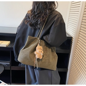 Detail of moss green suede tote bag with white stitching and plush dog charm accessory