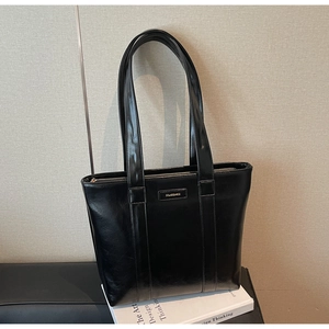 Détail d'un cabas noir brillant en similicuir avec plaque logo dorée et texture lisse