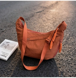 Detail of orange nylon crescent bag with wide strap and braided zipper pull outdoors