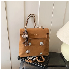 Détail d'un sac à dos marron mat avec écussons étoiles et poignée tissée sur livre