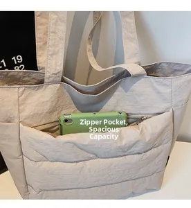 Detail view of beige quilted tote bag showing large front zipper pocket with phone storage