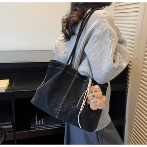 Detail of black suede tote bag with white contrast stitching and plush bear charm