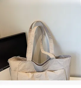 Detail of off-white tote bag showing crinkled nylon texture and multiple side pockets