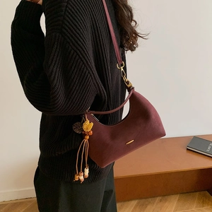 Detail of burgundy crescent crossbody bag with decorative tassel and golden logo bar