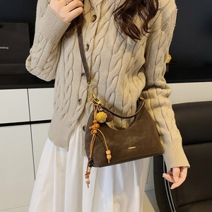 Detail view of coffee brown crescent bag with retro gold hardware and ethnic tassel charm