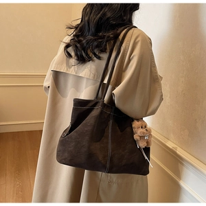 Detail of dark brown suede tote bag with contrast stitching and teddy bear charm