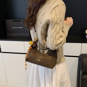 Detail of a brown suede crescent bag with fringe tassels on a beige sweater outfit