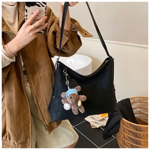 Detail of black embossed leather tote bag featuring a cute plush bear charm accessory
