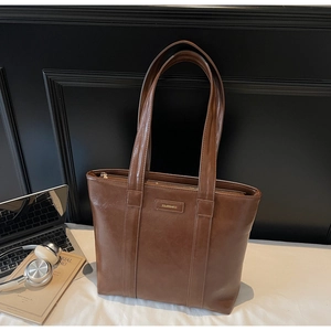 Détail d'un sac cabas en cuir marron avec logo métallique et sangles dans un décor de bureau