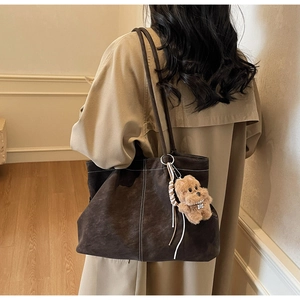Deep brown suede tote bag with white stitching detail and plush dog charm on shoulder