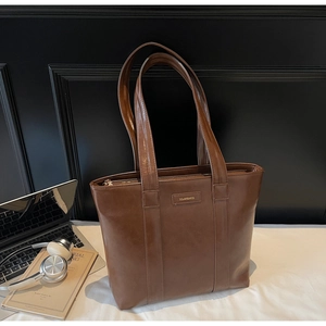 Détail d'un sac cabas en cuir marron avec logo sur un bureau avec ordinateur et casque