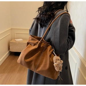 Detail of a brown suede tote bag with white stitching and a cute teddy bear charm