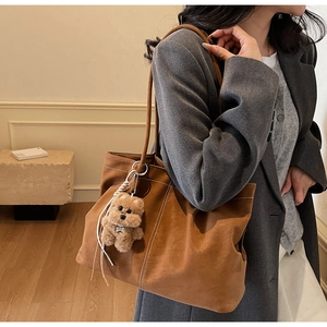 Brown tote bag with white contrast stitching and a plush bear charm worn by a model
