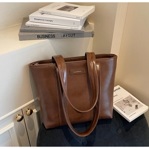 Détail du cabas en cuir marron foncé avec logo en métal sur un support en tissu doux