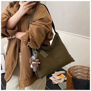 Detail of dark olive green tote bag featuring embossed floral patterns and a plush bear charm