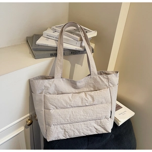 Macro detail of quilted beige nylon tote bag with side pockets on a minimal background