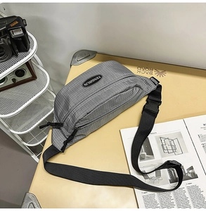 Macro shot of grey plaid nylon sling bag featuring adjustable strap and buckle on desk