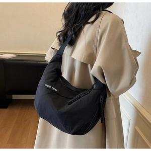 Detail view of black nylon crescent crossbody bag with white logo lettering on model