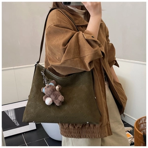 Detail of dark olive green tote bag with embossed logo and plush bear charm decoration