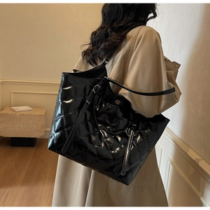 Detail of glossy black quilted tote bag showing fine diamond texture and adjustable strap