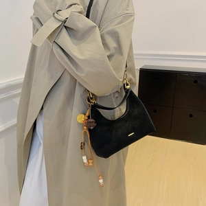 Detail of black suede hobo bag with ethnic charm and golden hardware on model
