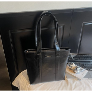 Détail du sac cabas noir brillant avec plaque de marque dorée et fermeture éclair robuste