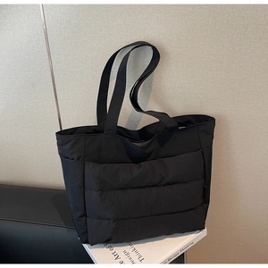Detail view of the quilted texture and wide shoulder strap on this black tote bag