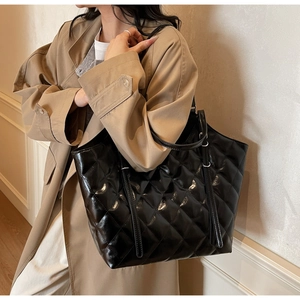 Vue détaillée du grand sac cabas noir matelassé brillant porté à l'épaule par un mannequin