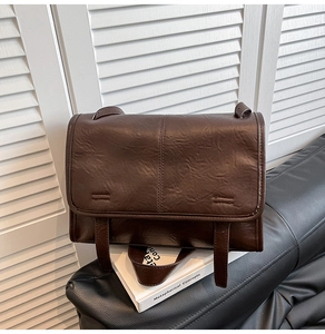 Close-up of the vintage brown faux leather crossbody bag on a sleek black leather sofa