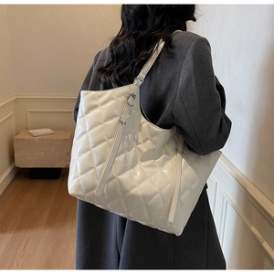 Close-up of the large quilted diamond pattern and adjustable strap on the cream tote bag