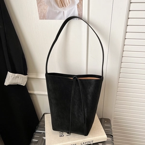 Detail of minimalist black leather bucket bag on a metallic suitcase in a modern office setting