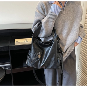 Model wearing a large black leather hobo bag with adjustable wide shoulder straps